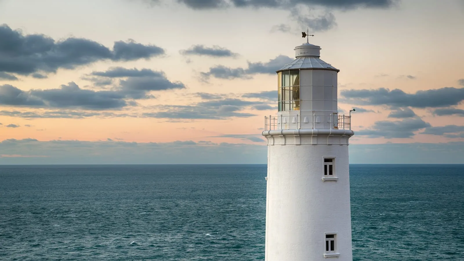 A white lighthouse on a headland above a calm sea at dusk