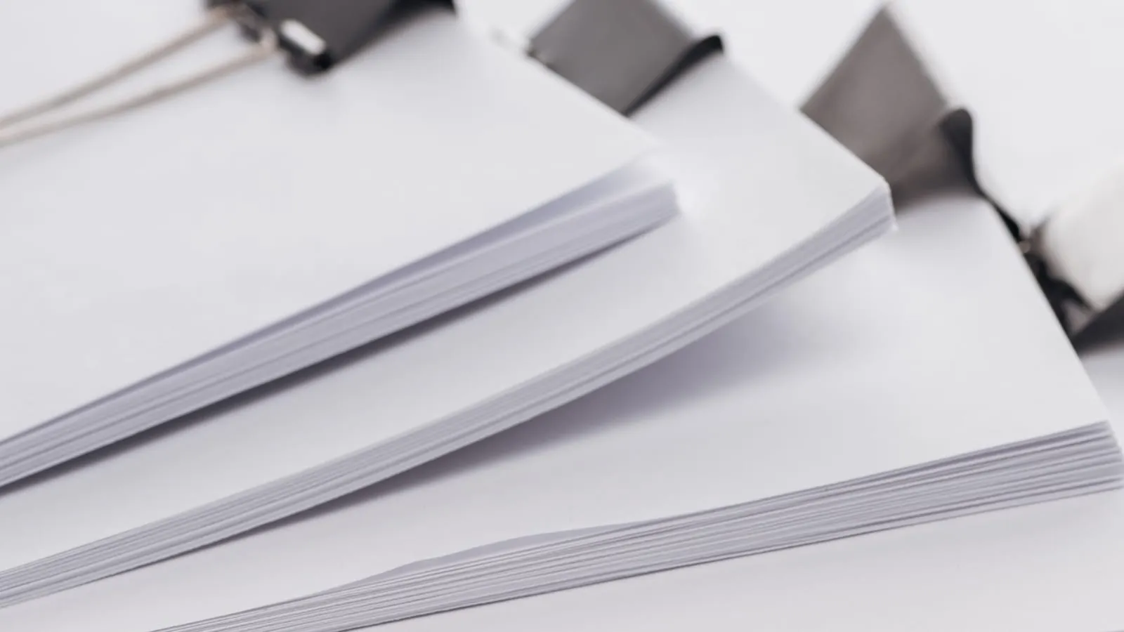 Three stacks of blank paper, each held together with a black binder clip