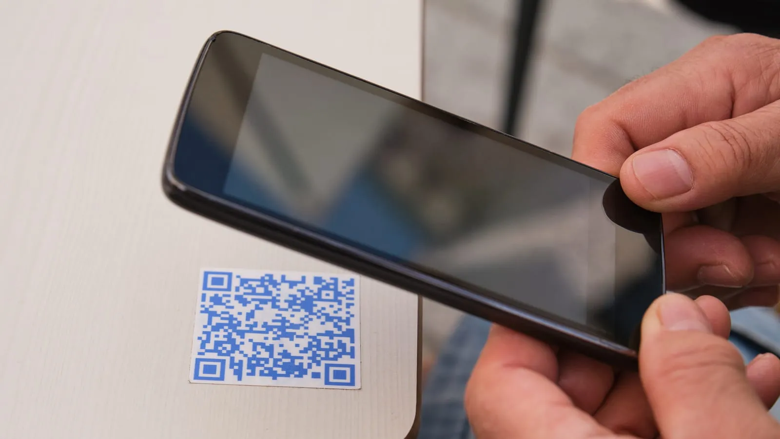 A hand holding a phone over a blue QR code sticker on a table