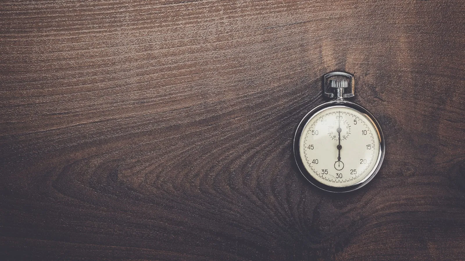 A silver stopwatch lying on a dark wooden surface