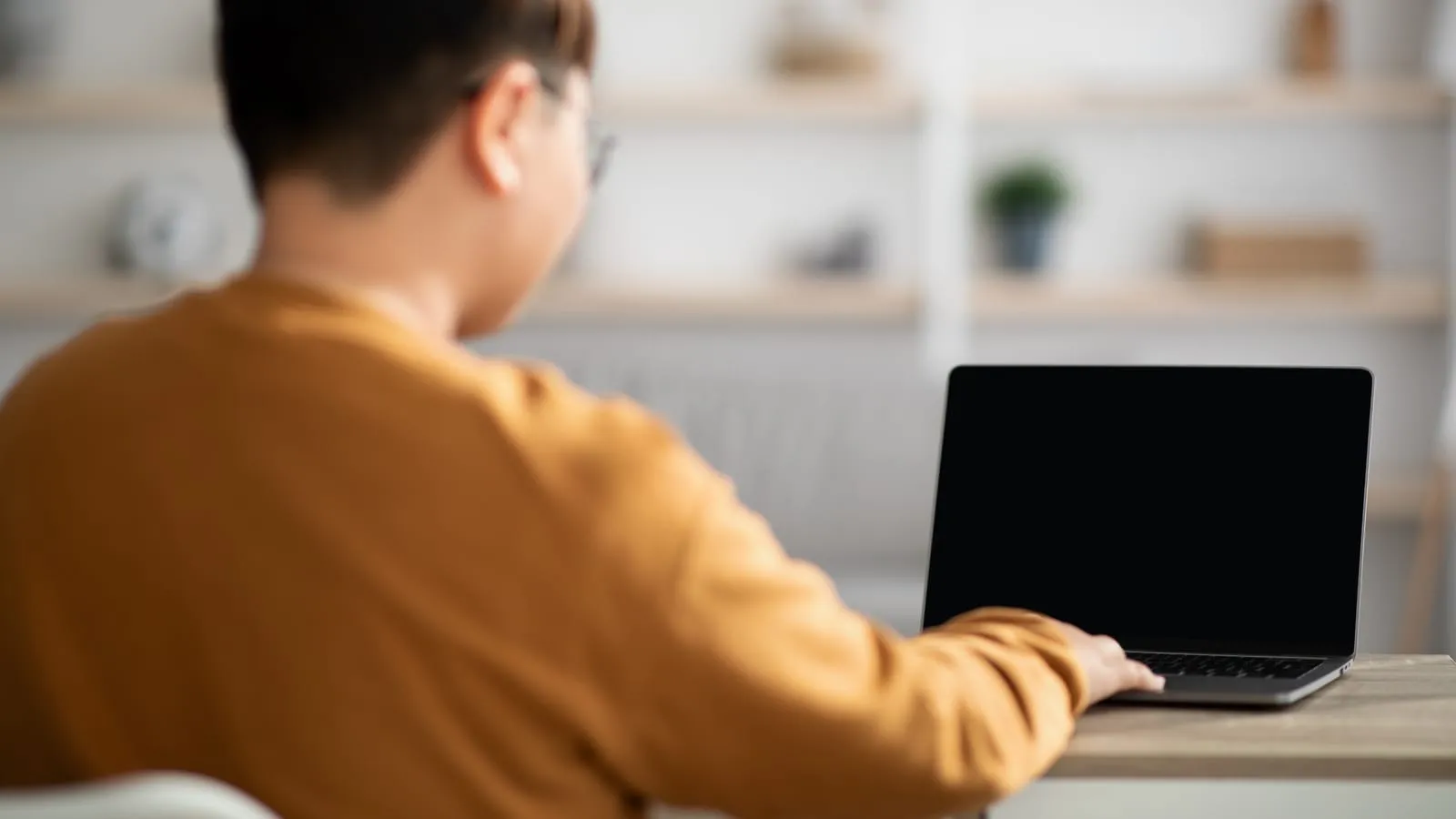 A person seen from behind at a desk, using a laptop with a dark screen