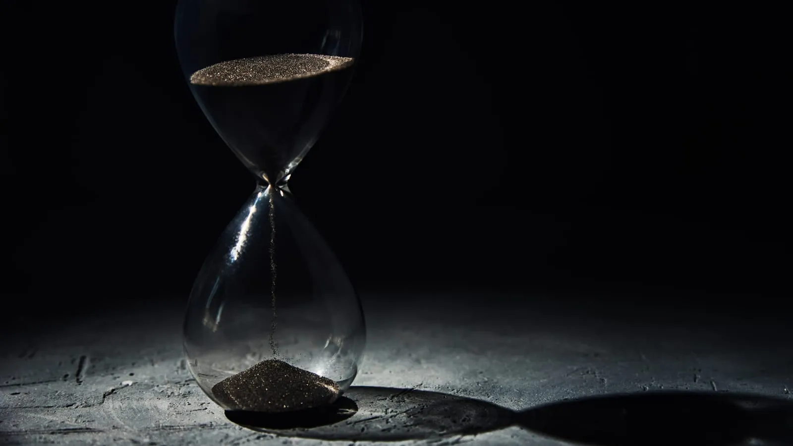 An hourglass running out of sand against a black background