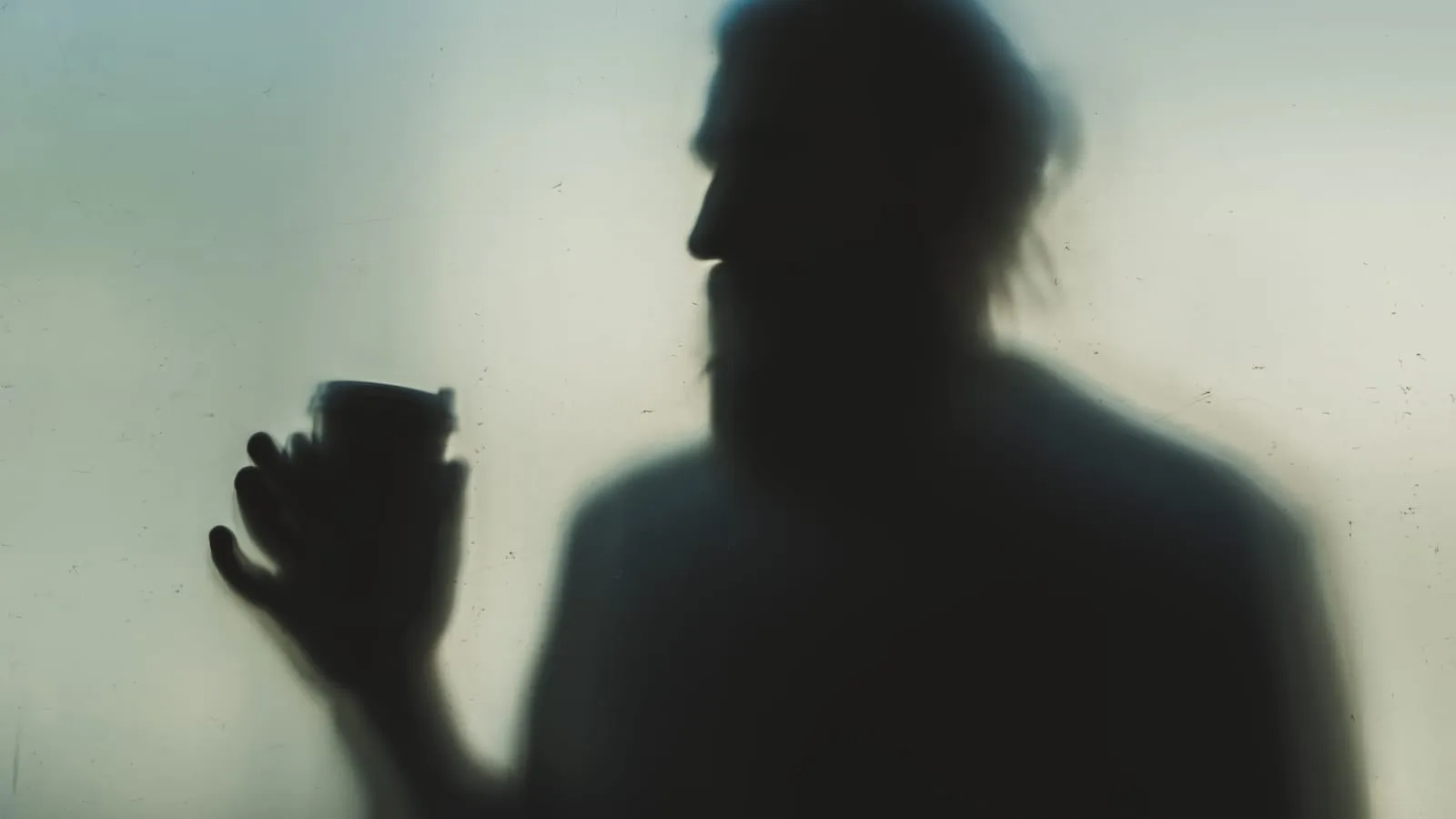 The blurred silhouette of a person holding a cup behind frosted glass