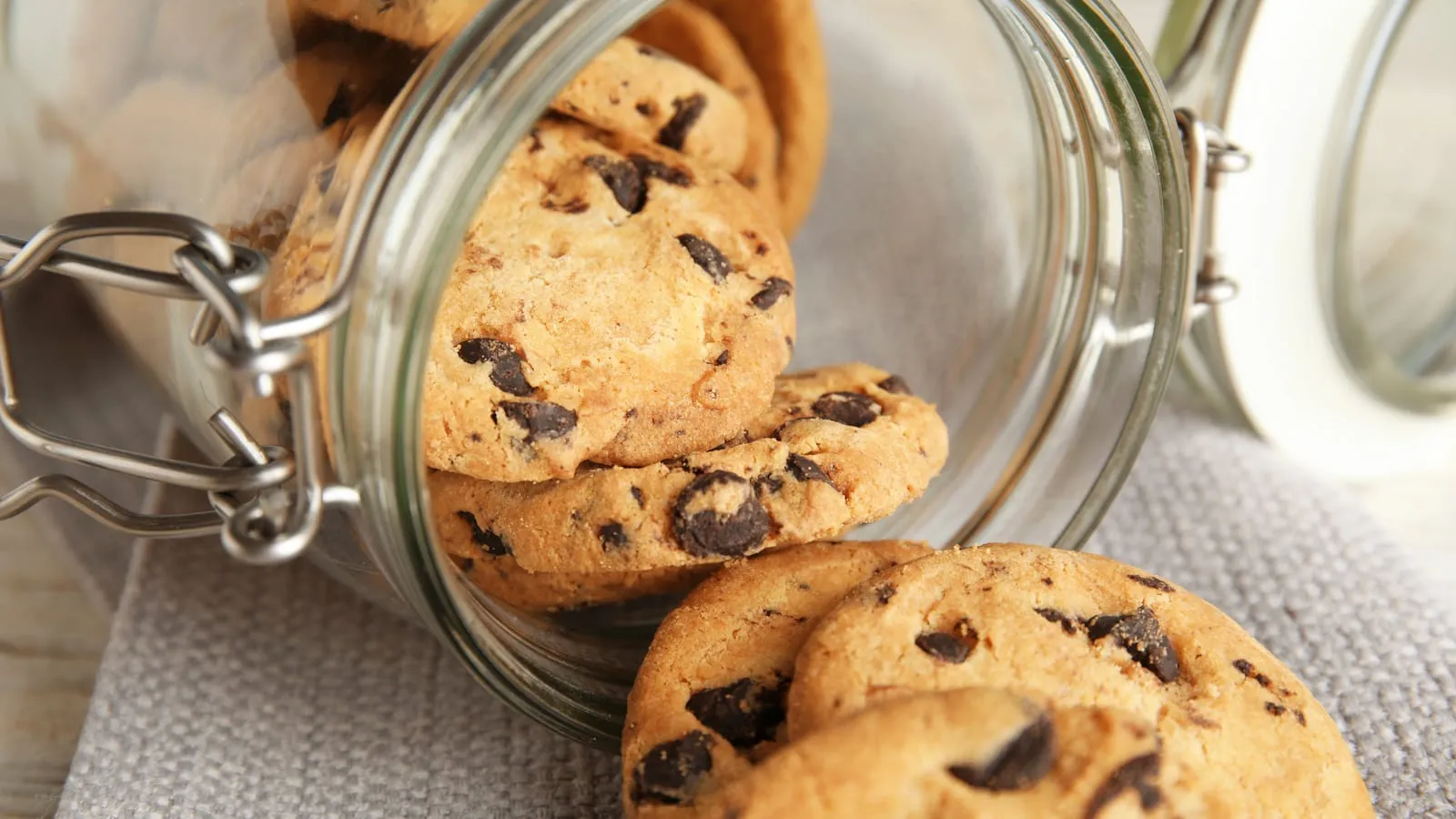 Chocolate chip cookies spilling out of a tipped-over glass jar